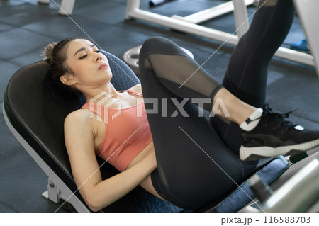 Young beautiful woman taking a rest after her leg push up exercise during her morning work out at a gym Young beautiful woman taking a rest after her leg push up exercise during her morning work out at a gym 116588703