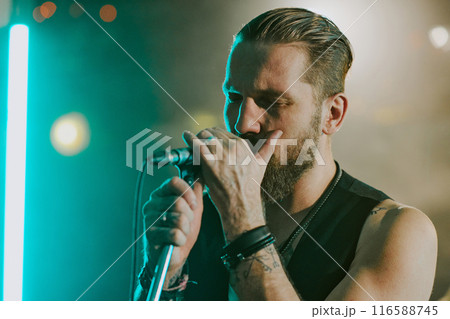 Medium closeup of Caucasian male musician singing emotional rock ballad with eyes closed on stage, copy space 116588745