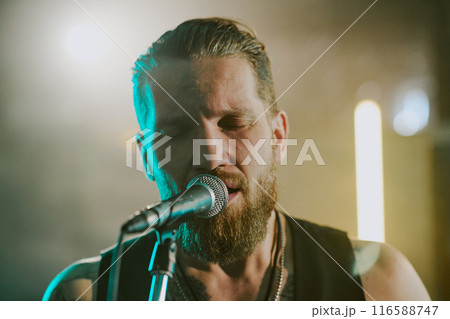 Closeup shot of professional rock vocalist singing ballad song with eyes closed on stage Closeup shot of professional rock vocalist singing ballad song with eyes closed on stage 116588747