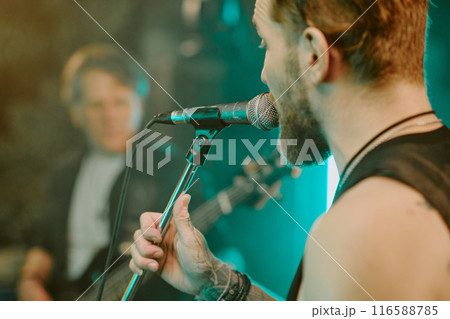 Closeup shot of young Caucasian male vocalist singing heavy metal song into microphone on stage Closeup shot of young Caucasian male vocalist singing heavy metal song into microphone on stage 116588785
