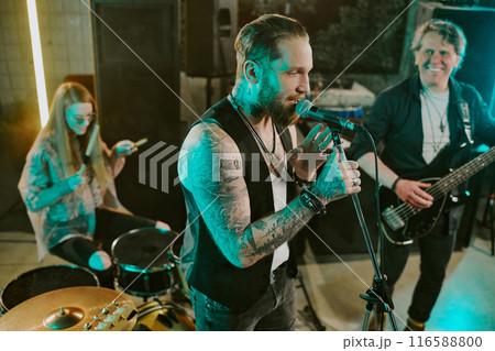 High angle view of Caucasian male vocalist, bassist and female drummer playing punk rock music on stage in bar 116588800