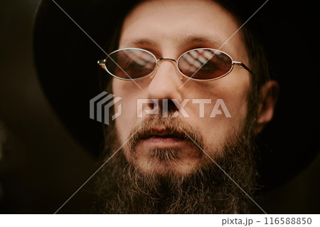 Closeup portrait of gen X Caucasian man with beard on face wearing hat and stylish sunglasses Closeup portrait of gen X Caucasian man with beard on face wearing hat and stylish sunglasses 116588850