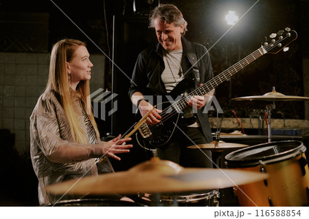 Joyful young female drummer and mature male bassist talking while having rehearsal in garage 116588854