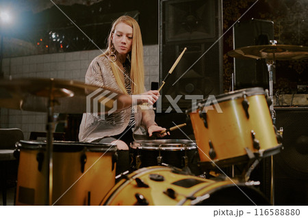 Young Caucasian female musician with long blond hair playing drums on stage in bar, copy space Young Caucasian female musician with long blond hair playing drums on stage in bar, copy space 116588880