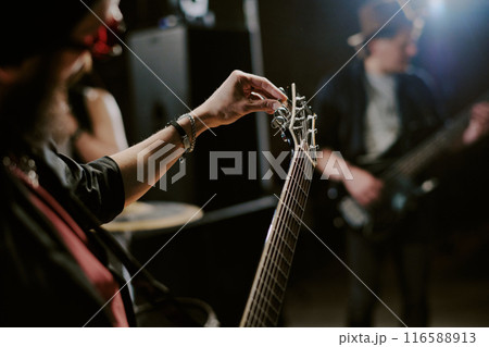 Medium closeup of unrecognizable bearded musician playing in rock band tuning electric guitar, copy space 116588913