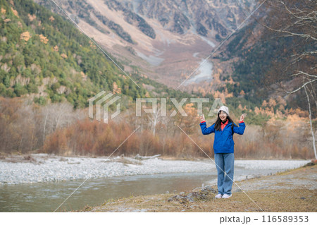 Excitement in nature, Asian woman in a blue jacket enjoys the orange hues of fall. A stylish traveler in Japan, standing alone, reflecting on the journey's joy. Excitement in nature, Asian woman in a blue jacket enjoys the orange hues of fall. A stylish traveler in Japan, standing alone, reflecting on the journey's joy. 116589353