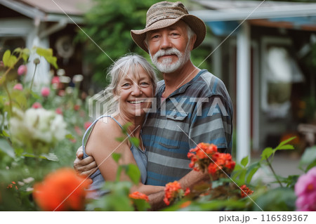 A happy senior couple hugging in their garden, surrounded by colorful flowers and greenery, enjoying a sunny day 116589367