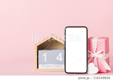 mobile phone with blank screen on colored background with hearts, calendar and gift box, valentine day 14 february concept perspertive view flat lay mobile phone with blank screen on colored background with hearts, calendar and gift box, valentine day 14 february concept perspertive view flat lay 116589608