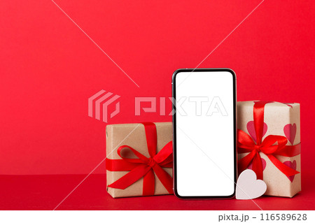 mobile phone with blank screen on colored background with hearts, calendar and gift box, valentine day concept perspertive view flat lay mobile phone with blank screen on colored background with hearts, calendar and gift box, valentine day concept perspertive view flat lay 116589628