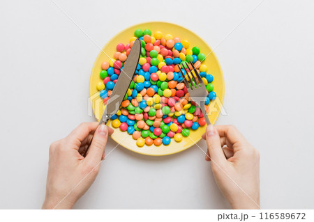 the girl holds cutlery in her hands and eats sweets in a plate. Health and obesity concept, top view on colored background 116589672