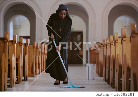 Long shot of young African American nun wiping floor at nave in Catholic church with use of mop, copy space 116592191
