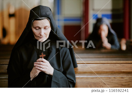 Selective focus shot of pious Catholic nun holding wooden cross in hands praying to Lord, copy space Selective focus shot of pious Catholic nun holding wooden cross in hands praying to Lord, copy space 116592241