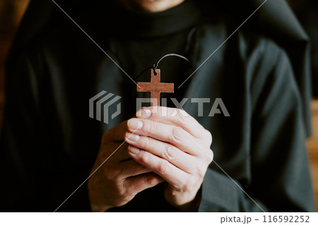 Closeup shot of hands of unrecognizable mature Catholic nun wearing black habit holding wooden cross Closeup shot of hands of unrecognizable mature Catholic nun wearing black habit holding wooden cross 116592252