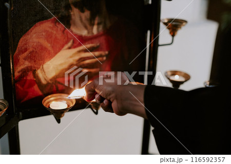 Hand of unrecognizable Catholic nun holding burning match lighting up candles in church Hand of unrecognizable Catholic nun holding burning match lighting up candles in church 116592357