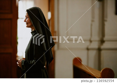 Medium side view shot of mature Caucasian nun wearing black religious habit standing in Catholic church, copy space Medium side view shot of mature Caucasian nun wearing black religious habit standing in Catholic church, copy space 116592554