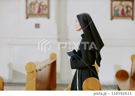 Side view medium shot of mature Caucasian Catholic nun walking along nave in church, copy space Side view medium shot of mature Caucasian Catholic nun walking along nave in church, copy space 116592613