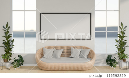A minimalist white living room features a wicker sofa, houseplants, and a frame mockup on the wall. 116592829