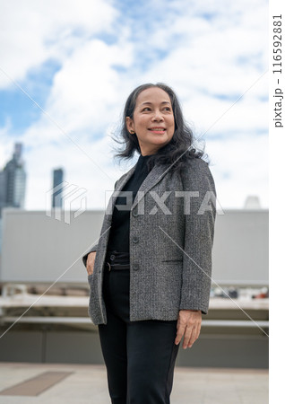 A confident, happy Asian senior businesswoman stands in the big urban city, looking at the sky. A confident, happy Asian senior businesswoman stands in the big urban city, looking at the sky. 116592881