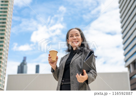 A confident Asian senior businesswoman stands in the urban city surrounded by skyscraper buildings. A confident Asian senior businesswoman stands in the urban city surrounded by skyscraper buildings. 116592887