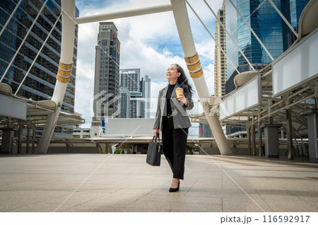 A successful mature Asian businesswoman walking in the city with her takeaway coffee and a briefcase A successful mature Asian businesswoman walking in the city with her takeaway coffee and a briefcase 116592917