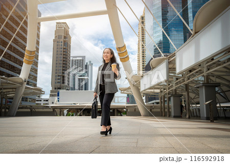 A confident, happy mature Asian businesswoman is commuting to work, walking in the city. A confident, happy mature Asian businesswoman is commuting to work, walking in the city. 116592918