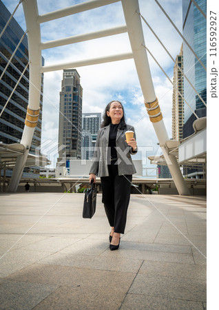 A confident mature Asian businesswoman in a suit is walking in the city, commuting to her office. A confident mature Asian businesswoman in a suit is walking in the city, commuting to her office. 116592927
