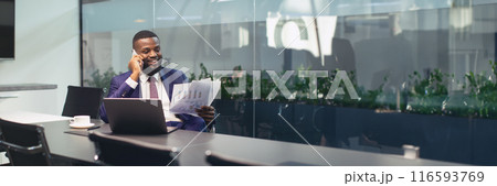 Happy young black businessman having phone conversation with assistant or business partner, sitting at table in front of laptop, holding papers, drinking coffee, working at conference hall, copy space Happy young black businessman having phone conversation with assistant or business partner, sitting at table in front of laptop, holding papers, drinking coffee, working at conference hall, copy space 116593769