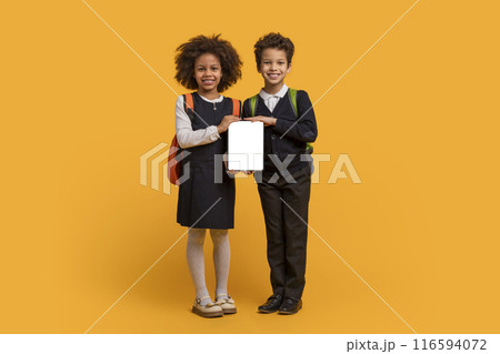 Two young students, African American boy and girl, are standing side by side, holding a blank tablet in front of them. The children are possibly working on a project Two young students, African American boy and girl, are standing side by side, holding a blank tablet in front of them. The children are possibly working on a project 116594072