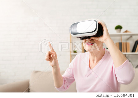 Senior woman wearing a pink shirt is focused on using a virtual device. She is interacting with the screen, presumably engaged in a digital task or activity, closeup, copy space 116594301