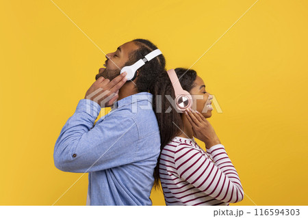 African American man and woman are shown wearing headphones, listening to music. They appear focused on their music, possibly enjoying the sound quality. 116594303