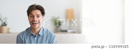 Excited handsome young man smiling at camera, enjoying weekend or vacation, home interior, panorama with copy space 116594585