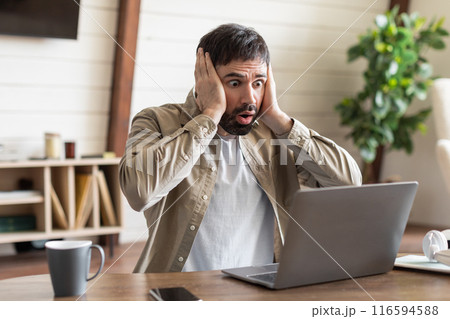 A man is seated in front of a laptop with a look of concentration, holding his head in frustration or contemplation. He appears to be deep in thought or experiencing some sort of mental strain. 116594588