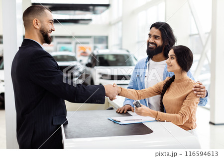 A man and a woman are shaking hands inside a well-lit car showroom. The man appears to be a car salesman, and Indian woman is a potential customer. They are standing next to a shiny car A man and a woman are shaking hands inside a well-lit car showroom. The man appears to be a car salesman, and Indian woman is a potential customer. They are standing next to a shiny car 116594613