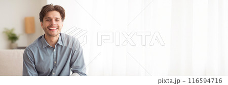 Cheerful Handsome Young Man Smiling At Camera Sitting On Couch At Home. Empty Space For Text, Web-banner 116594716
