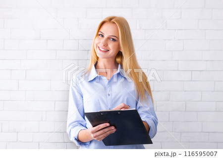 A woman wearing a blue shirt is seen holding a clipboard in her hands. She appears focused and engaged, possibly working or taking notes. The background is simple and nondescript. A woman wearing a blue shirt is seen holding a clipboard in her hands. She appears focused and engaged, possibly working or taking notes. The background is simple and nondescript. 116595007