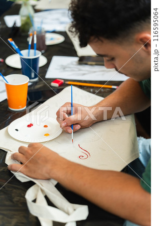 Back shot of a boy painting with a paintbrush at a summer activity with his friends. Vertical 116595064