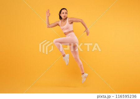 A woman wearing a pink outfit is captured mid-air as she jumps energetically. Her arms are outstretched and her legs are bent, showcasing a moment of dynamic movement and joy. A woman wearing a pink outfit is captured mid-air as she jumps energetically. Her arms are outstretched and her legs are bent, showcasing a moment of dynamic movement and joy. 116595236
