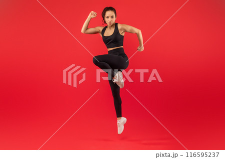 A fitness instructor is captured mid-motion while performing a high-knee exercise, showcasing her strength and agility. She is dressed in athletic wear and appears focused and determined 116595237