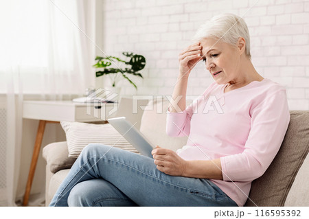 Confused senior woman using tablet computer, looking disappointed, doesn't understand modern gadgets, empty space 116595392