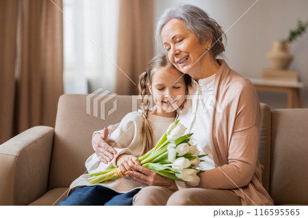A tender moment is captured as a smiling grandmother wraps her arms around her young granddaughter, who is holding a bouquet of fresh tulips 116595565