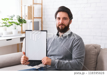 Confident psychotherapist showing white blank clipboard at camera, sitting in office, free space for announcement Confident psychotherapist showing white blank clipboard at camera, sitting in office, free space for announcement 116595828