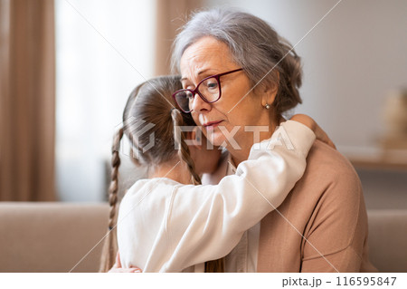 A tender moment between a grandmother and her granddaughter as they embrace in a gentle hug. The grandmother gazes thoughtfully into the distance, her expression a mix of affection and contemplation 116595847