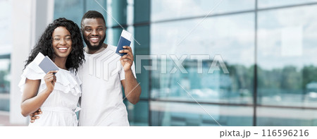 A happy, young black couple stands in front of an airport window, holding their boarding passes in anticipation of their upcoming trip, panorama with copy space A happy, young black couple stands in front of an airport window, holding their boarding passes in anticipation of their upcoming trip, panorama with copy space 116596216
