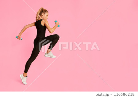 Sporty Millennial Girl Jumping With Dumbbells During Workout Training On Yellow Background In Studio. Full Length Sporty Millennial Girl Jumping With Dumbbells During Workout Training On Yellow Background In Studio. Full Length 116596219