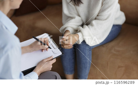 Unrecognizable Psychologist Talking With Female Client Taking Notes During Psychotherapy Session Sitting In Office. Selective Focus, Cropped 116596289