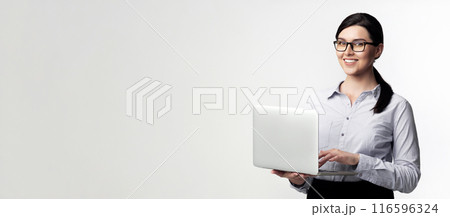 A smiling businesswoman in a white shirt holds a laptop in front of a white background. 116596324