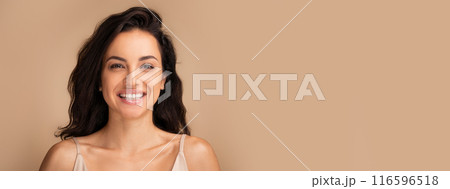 Cheerful attractive young woman with long black hair posing on beige studio background, wearing top, panorama with copy space 116596518