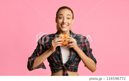 Cheat Meal Concept. Millennial Girl Eating Burger Over Yellow Background In Studio. Empty Space For Text Cheat Meal Concept. Millennial Girl Eating Burger Over Yellow Background In Studio. Empty Space For Text 116596772