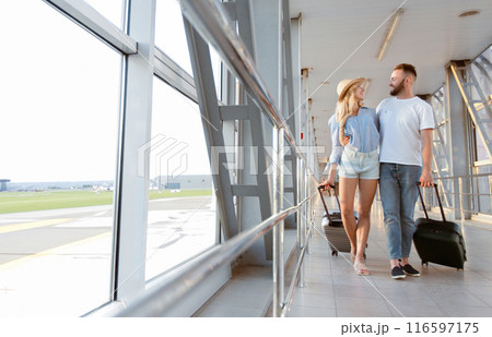 Romantic Travel. Loving couple walking with luggage in airport, hugging and looking at each other, copy space 116597175