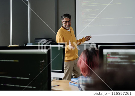Modern mature teacher of Computer Science standing in front of students in modern classroom and conducting lesson 116597261